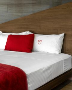 Contemporary hotel room interior featuring a cozy bed with red accents and heart embroidery in Ciudad de México.