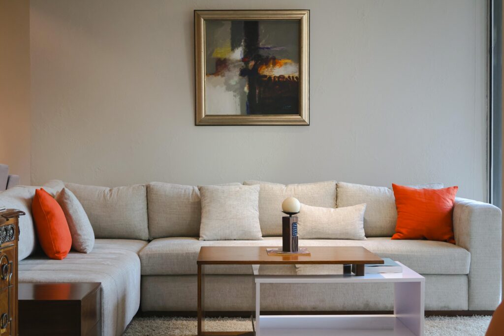 Contemporary living room with beige sofa, orange pillows, and abstract artwork.