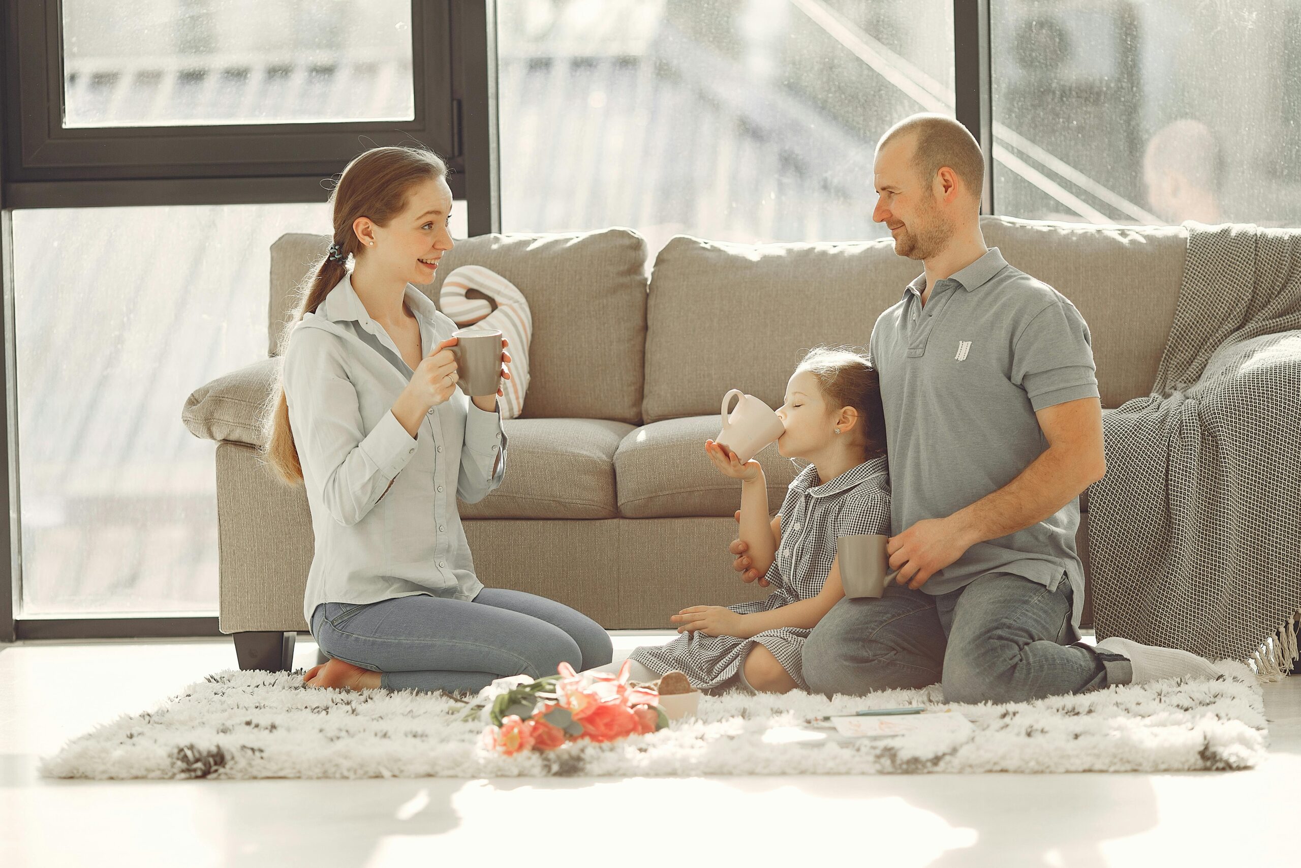 Cheerful family drinking tea in living room while having rest and laughing together during weekend while spending time and having fun