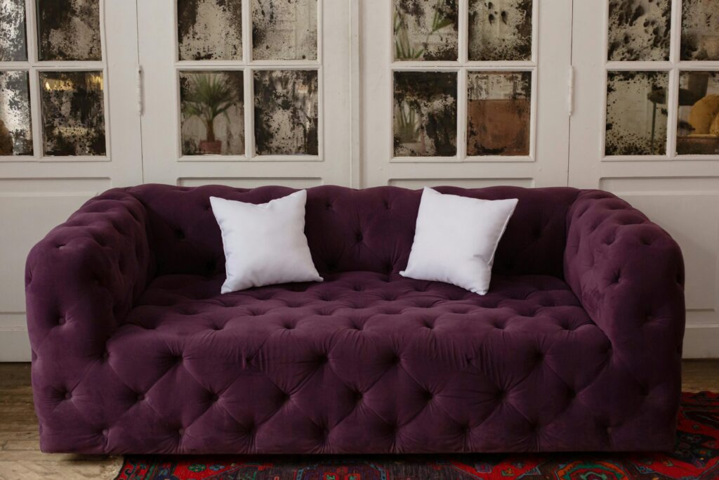 Luxurious purple tufted sofa with white cushions in a stylish, cozy indoor setting.