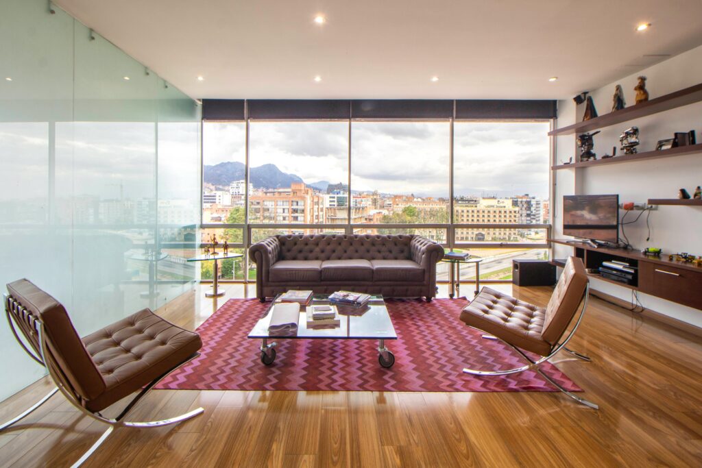 A stylish, minimalist living room featuring large windows, modern furniture, and a cityscape view.