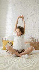 A young girl stretches on her bed with a stuffed toy beside, embracing the morning light.